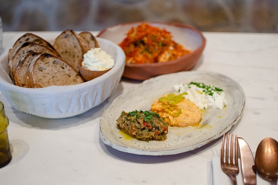 A basket of thick-cut sourdough bread is accompanied by thick butter and a trio of Greek spreads.