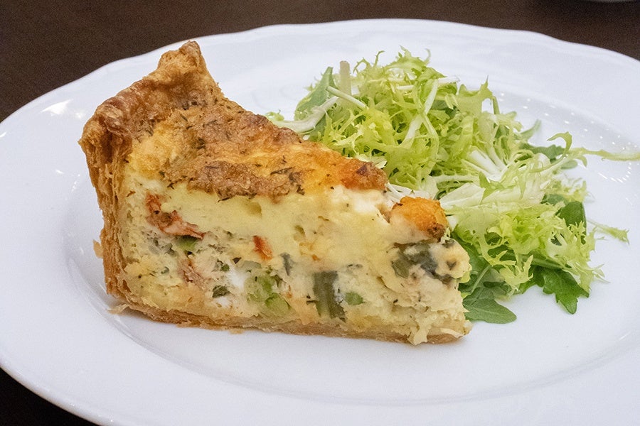 A pie slice-shaped wedge of quiche sits on a white plate next to greens.