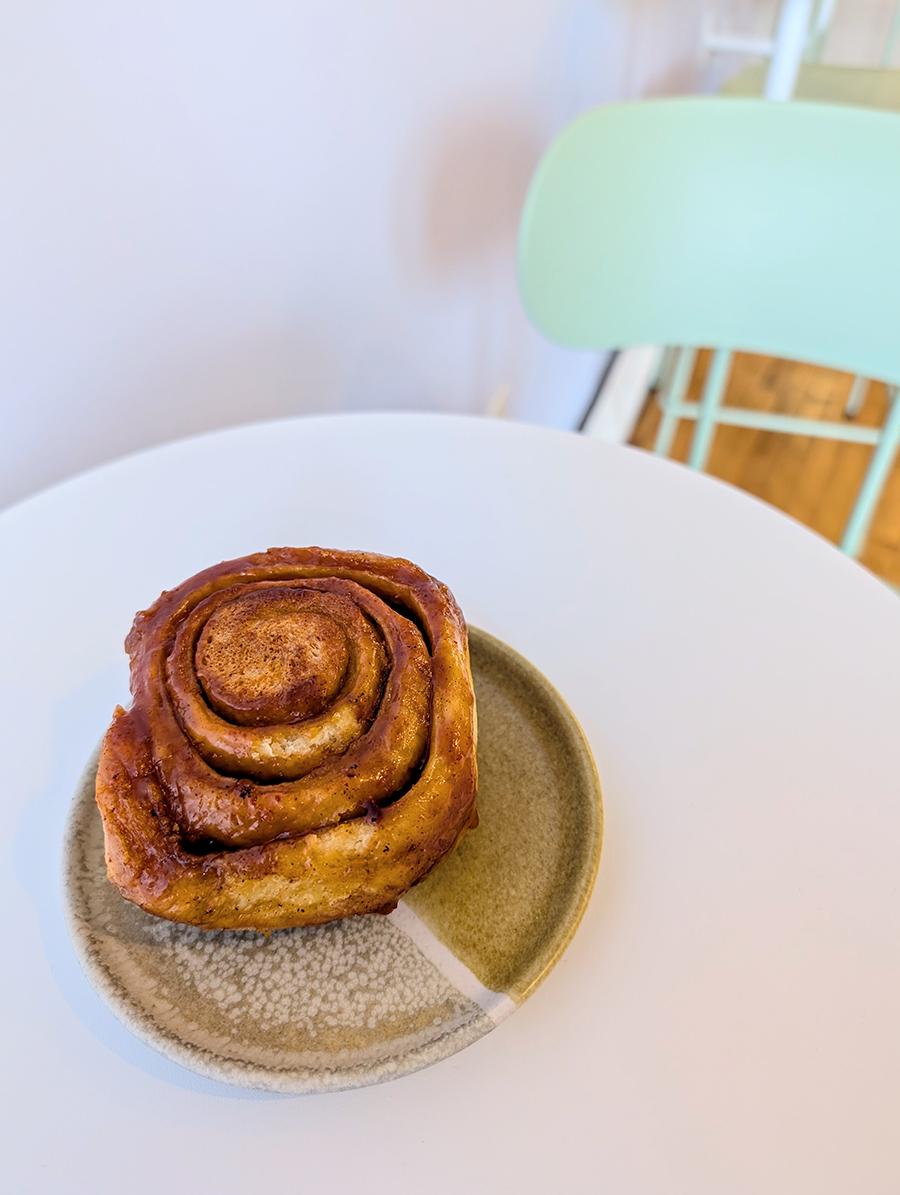 A sticky bun sits on a white table with a pastel green chair nearby.