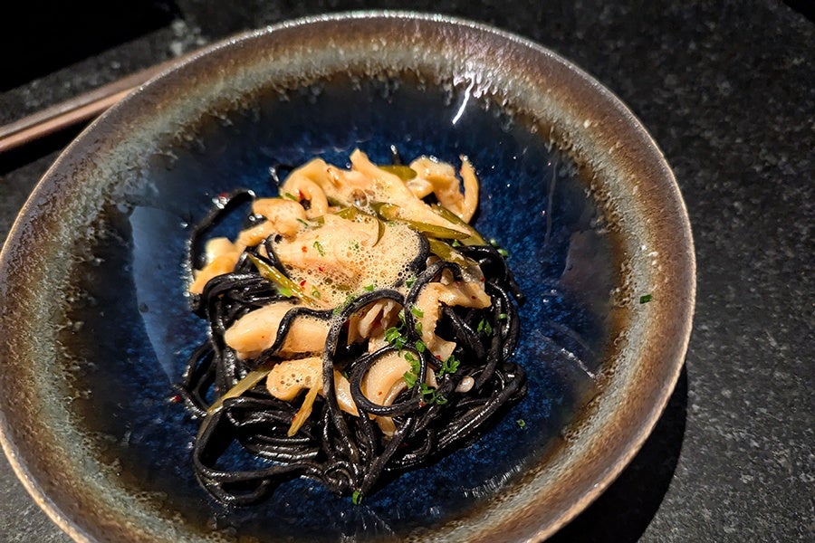 A bowl of black noodles with bits of shellfish and herbs.