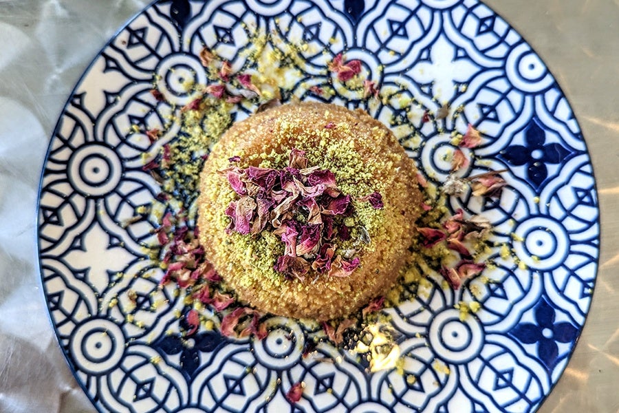 Overhead view of a Middle Eastern pastry dusted with a crumbled pistachio and rose petal topping.